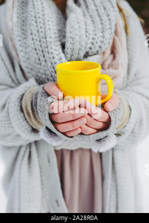 Boho fille portant doux tissé chandail est à l'extérieur en hiver et tient une tasse jaune de boisson chaude dans ses mains. Faible profondeur de champ. Banque D'Images