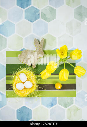 Décorations de Pâques colorées sur une table, œufs de poulet dans un nid, tulipes jaunes dans un vase blanc. Banque D'Images