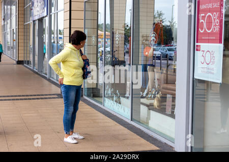 Une femme d'âge moyen seul regardant les marchandises dans un magasin fenêtre, window shopping Banque D'Images