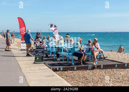 Touristes assis sur des bancs devant un café au bord de mer dégustez des glaces et de la nourriture par une chaude journée d'été À Bognor West Sussex Banque D'Images