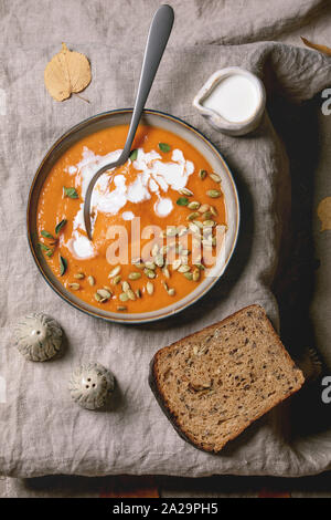 Soupe de potiron à la crème et les graines dans un bol en céramique sur toile, servi avec pain de seigle et de l'ail, les feuilles d'automne plus de brown texture background. Télévision Banque D'Images