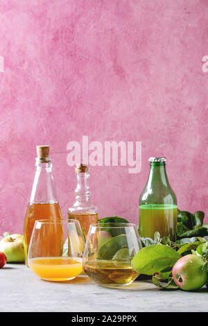 Variété de boissons d'Apple. Bouteilles verres d'ang le jus de pomme, le vinaigre de cidre de pommes et le jardin avec des feuilles et branches sur table avec pink backgrou Banque D'Images