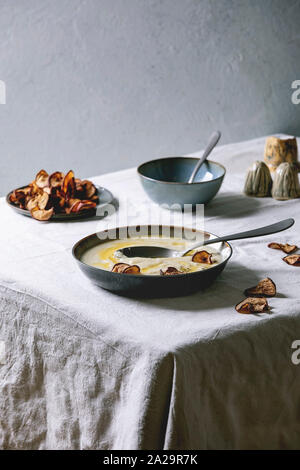 Chou-fleur soupe crème de panais ou Bol en céramique avec du beurre dans la sauce, bien Les poires séchées et d'herbes sur table de cuisine avec nappe blanche Banque D'Images