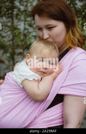Jeune rousse portage mère porter son sommeil d'un an bébé fille dans une rose wrap sling Banque D'Images