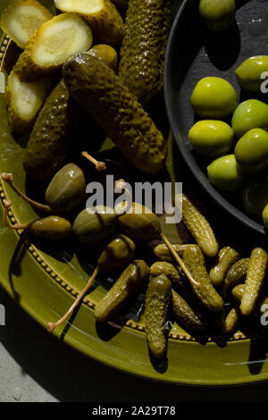 Une sélection de cornichons au vinaigre, olives vertes et câpres petits fruits sur une plaque de vert olive. Banque D'Images