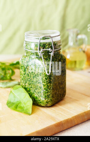 Sauce au pesto fait maison dans un bocal en verre avec le basilic, les ingrédients et baguette sur le tableau blanc dans la cuisine. Sauce au pesto - la cuisine italienne traditionnelle pour Banque D'Images