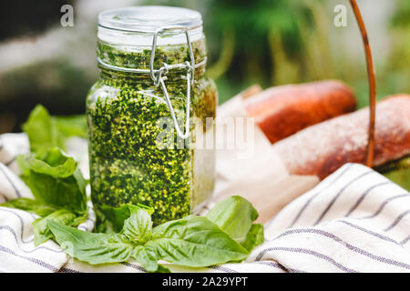 Le pesto dans un bocal de verre dans un panier de pique-nique en plein air. - Pesto sauce italienne pour les pâtes, pizza, focaccia, toasts, sandwichs, bruschetta. Banque D'Images