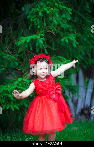 Une petite fille dans une belle robe rouge. Lovely baby posant sur la toile de fond de la forêt. Portre est une douce jeune fille. Banque D'Images