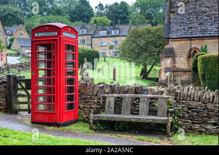 Cabine téléphonique rouge anglais typique médiévale à l'église anglicane St Barnabas avec mur de pierre et de cimetière gate de Snowshill, Cotswolds, Gloucestershire Banque D'Images