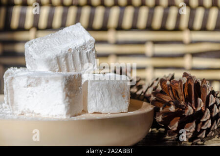 Délicieux blanc bulgare traditionnel loukoum sur plat en bois saupoudrée de sucre glace comme la neige. Douceurs orientales pour le thé, à côté des pommes de pin Banque D'Images