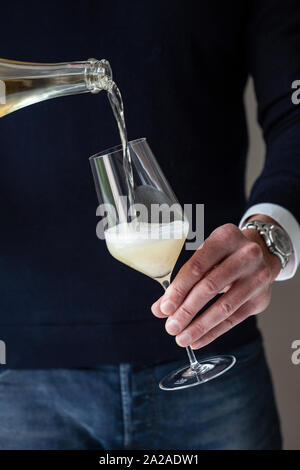 Un homme portant un haut noir et un jean verse du vin mousseux dans un verre Banque D'Images