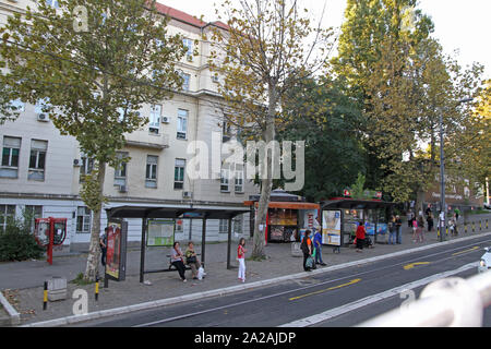 Groupe de personnes à l'arrêt de bus à l'extérieur d'un bâtiment blanc, Belgrade, Serbie. Banque D'Images