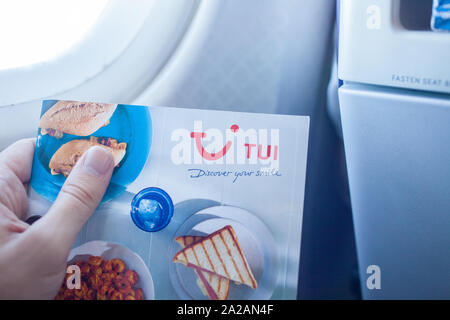 Menu en vol montrant la marque TUI à bord d'un avion. Close-up de la marque à l'intérieur de la cabine à l'aide d'un éclairage naturel. Homme tenant le menu. Banque D'Images