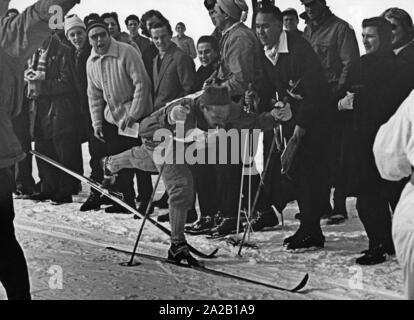 La photo montre un participant du 30 km ski de fond aux Jeux Olympiques d'hiver de 1956 à Cortina d'Ampezzo. Veikko Hakulinen c'est de la Finlande, qui a aussi gagné la médaille d'or à cette course. La ligne d'arrivée est entouré par la presse et fans qui sont l'encourageant. Banque D'Images