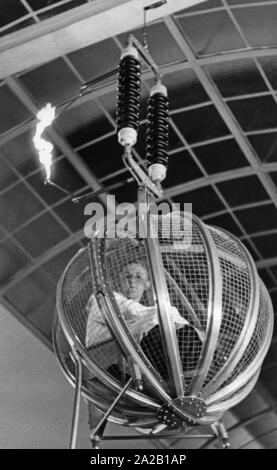 La photo montre un homme dans une cage de Faraday. Au cours de cette présentation de l'expérience au Deutsches Museum de Munich, un fort éclairage artificiel est déclenché, mais ne touche pas la personne assise dans la cage. La cage de Faraday protège l'intérieur (par exemple, la foudre dans une voiture ou en avion). Banque D'Images