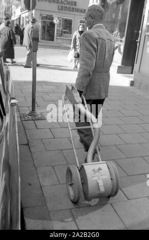 Deux fonctionnaires de vider les parcomètres installés dans le centre-ville de Munich. Après l'ouverture du parking meter les pièces tombent dans le petit coffre-fort mobile, grâce à une sorte de tuyau en plastique. L'ensemble de la construction n'est pas sans rappeler un sac chariot. Les parcomètres était de plus en plus souvent mis en place à Munich pour l'interdiction des parkers à long terme du centre-ville depuis le milieu des années 1950. Photo d'un fonctionnaire sur son chemin à l'autre parking meter avec le mobile coffre-fort. Banque D'Images