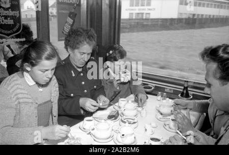 Photo de la ligne de train sur le Leipzig-Gutenfuerst Hof-Munich-route. Ce train était connu pour ses 'allemande' tout-voiture-restaurant, qui a été populaire en raison de la 1 : 1 taux de change, en particulier parmi les voyageurs de l'Allemagne de l'Est. Photo de train de boire du café et manger des gâteaux dans la voiture-restaurant. L'Allemagne de l'employé de chemin de fer (à gauche) avec ses deux enfants assis à la table avec une femme de Munich et un étudiant du village. Banque D'Images