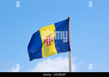 Waving Flag de Madère avec ciel bleu en arrière-plan. Il se compose d'un blue-or-bleu avec une croix rouge triband vertical-bordé blanc Croix du Christ au centre. Île portugaise dans l'océan Atlantique. Banque D'Images