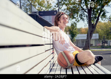 Photo de l'homme sportif avec volley-ball ball assis sur banc en bois sur la journée d'été Banque D'Images