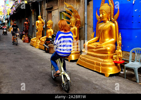 Femme sur un vélo en face de statues de Bouddha en or Bamrung Mueang Road, Bangkok, Thaïlande Banque D'Images