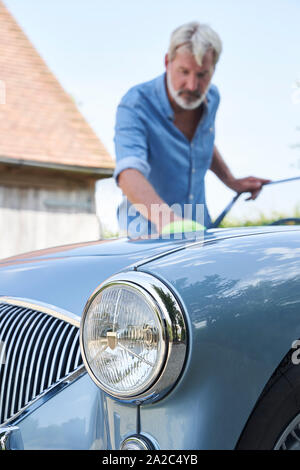 Homme mature restauré Polissage Voiture de sport classique dehors à la maison Banque D'Images