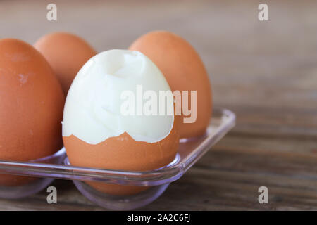 Close up six oeufs brun dans un coffret plastique sur table en bambou avec un oeuf cassé. Banque D'Images