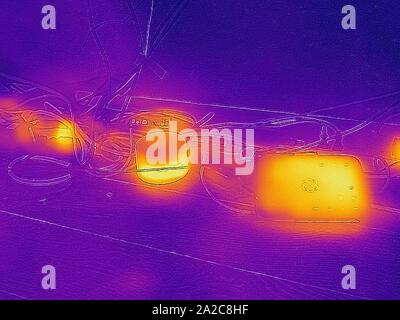 Image thermographique de caméra thermique, avec zones lumineuses correspondant à des températures plus élevées, montrant la chaleur résiduelle générée par les appareils électroniques inactifs, y compris (L à R) un adaptateur secteur, un routeur Google Wifi, Et Ooma Phone Hub, un exemple de charge fantôme ou de perte de puissance de secours, appelé colloque sur la puissance vampire ou la charge fantôme, San Ramon, Californie, septembre 2019. () Banque D'Images