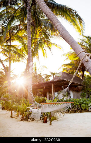 Hamac entre palmiers tropicaux sur la plage de sable blanc au coucher du soleil Banque D'Images