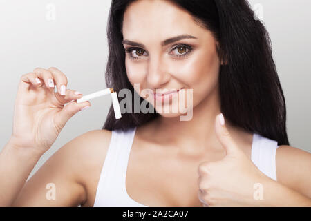 Jeune femme, confiante. Arrête de fumer. C'est avec une cigarette brisée sur un fond gris. Le concept est la lutte contre le tabagisme. Health Banque D'Images