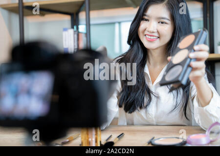 Belle femme asiatique blogger est montrant comment faire et l'utilisation des cosmétiques. En face de la caméra à l'enregistrement de vidéo en direct en streaming vidéo à la maison.Busin Banque D'Images