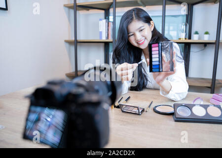 Belle femme asiatique blogger est montrant comment faire et l'utilisation des cosmétiques. En face de la caméra à l'enregistrement de vidéo en direct en streaming vidéo à la maison.Busin Banque D'Images