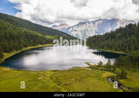 Photo prise avec un drone au-dessus du lac de montagne plongée dans les bois avec abri et les Alpes en arrière-plan Banque D'Images