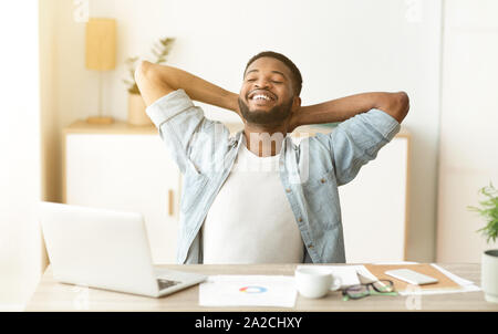 Heureux travailleur afro se pencher en arrière dans la chaise après journée réussie Banque D'Images