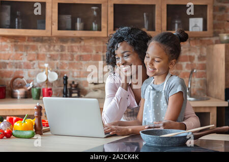 Maman et sa fille lecture fiche sur ordinateur portable à la cuisine Banque D'Images