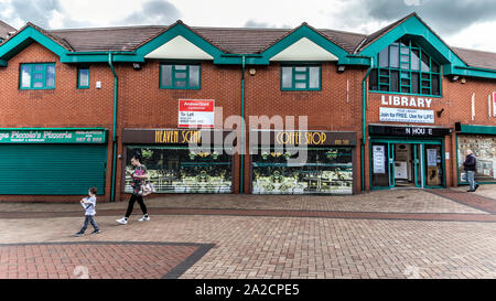 Femme âgée marcher passé fermé boutiques dans la zone piétonne sont de Tipton, au nord-ouest de Birmingham, West Midlands, Royaume-Uni, avec une propriété commerciale je signe dans l'arrière-plan. Banque D'Images