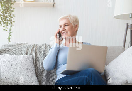 Senior woman holding laptop modernes et de parler par téléphone Banque D'Images