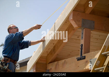 Constructeur mâle tenant un ruban de mesure sur une maison en construction. Banque D'Images