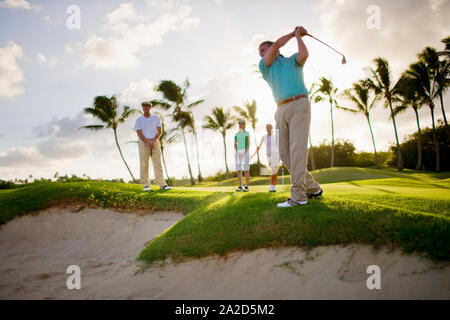 Homme et deux femmes regarder un golfeur mâle prendre un coup plus d'une fosse de sable. Banque D'Images