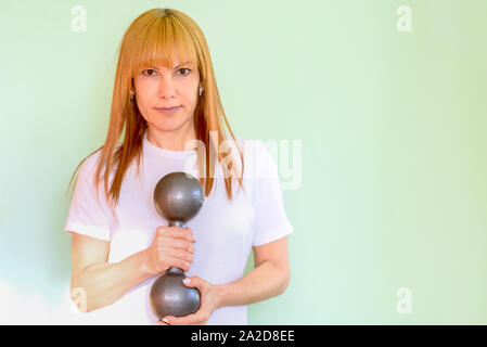 Happy middle aged woman lifting dumbbells fitness smiling et énergique sur fond vert menthe neo. Banque D'Images