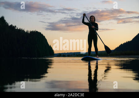 Fille d'aventure sur un Paddle Board est une pataugeoire dans un lac calme avec des montagnes en arrière-plan pendant un été haut en couleurs du coucher du soleil. Prises dans le lac Stave sw Banque D'Images