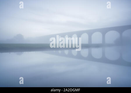 L'esquisse de Arthington viaduc est visible dans la fin de l'automne épais brouillard, reflétée dans les eaux vives du calmement River Wharfe avant le lever du soleil. Banque D'Images