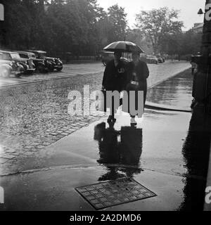 Zwei Frauen im Regen unter einem Regenschirm, Deutschland 1930 er Jahre. Deux femmes dans la pluie sous un parapluie, Allemagne 1930. Banque D'Images