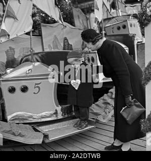 Ein kleiner Junge steht mit senneur Mutter suis Kinderkarussell auf dem Weihnachtsmarkt Deutschland, 1930er Jahre. Un petit garçon et sa mère debout par un carrousel kiddy au marché de noël, Allemagne 1930. Banque D'Images
