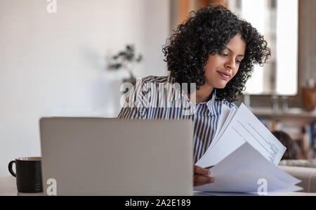 Souriante jeune femme entrepreneur passe plus de paperasse à la maison Banque D'Images