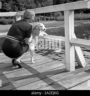 Eine junge Frau mit ihrem Foxterrier steht auf dem Steg une einem Voir, Deutschland 1930 er Jahre. Une jeune femme avec son chien fox terrier à quai sur un lac, l'Allemagne des années 1930. Banque D'Images