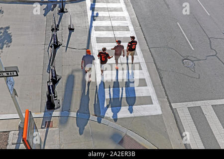 Cleveland Browns quatre fans de football, traverser une rue avant d'un jeu de nuit casting shadows par le soleil couchant dans le centre-ville de Cleveland, Ohio, USA. Banque D'Images