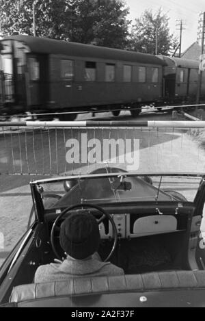 Eine junge Frau im 733wartet auf das von Vorbeifahren des Zuges un im Donautal Schranke, Deutschland 1930 er Jahre. Une jeune femme au volant d'une décapotable est attendant le train de passer dans un bar dans le Danube Dale, Allemagne 1930. Banque D'Images