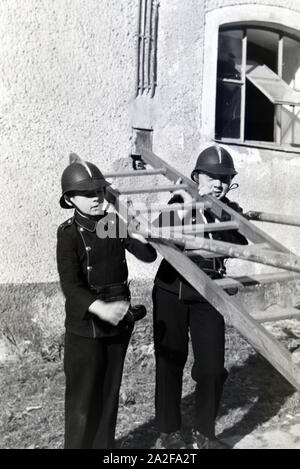 Zwei uniformierte Kinderfeuerwehr von der jungen halten die Leiter bei einer Feuerwehrübung, 1930er Jahre Deutschland. Deux garçons en uniforme des pompiers juniors sont titulaires d'un bain au cours d'une formation de pompier, Allemagne 1930. Banque D'Images