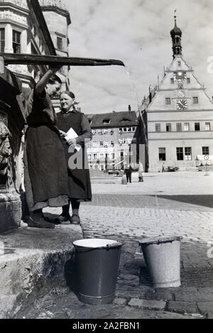 Zwei Frauen verwalten sich während Sie die Wassereimer mit Wasser aus dem Springbrunnen Am Marktplatz vor dem Rathaus und der Ratstrinkstube voll laufen lassen, Rothenburg ob der Tauber, Allemagne Allemagne Années 1930 er Jahre. Deux femmes ayant un chat tandis que le bucktes sont remplissage avec de l'eau de la fontaine sur la place du marché à proximité de la mairie et Ratstrinkstube à Rothenburg ob der Tauber, Allemagne 1930. Banque D'Images