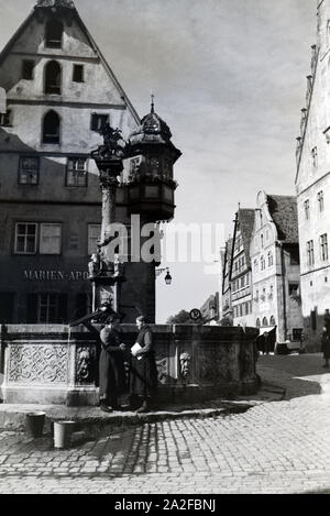 Zwei Frauen verwalten sich während Sie die Wassereimer mit Wasser aus dem Springbrunnen vor dem Rathaus imposanten voll laufen lassen, Rothenburg ob der Tauber, Allemagne Allemagne Années 1930 er Jahre. Deux femmes ayant un chat tandis que le bucktes sont remplissage avec de l'eau de la fontaine placée en face de l'impressionnant hôtel de ville de Rothenburg ob der Tauber, Allemagne 1930. Banque D'Images